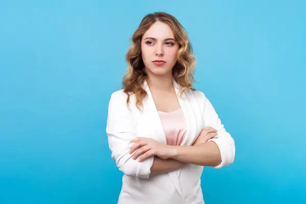 stock image Portrait of successful confident intelligent blond woman with wavy hair standing looking away keeps arms folded, wearing white shirt. Indoor studio shot isolated on blue background.