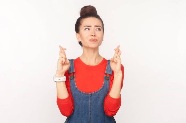 Saçları topuz gibi olmuş umut dolu bir kadının portresi şans dileyerek, dilek tutarak, kot pantolon giyerek parmaklarını çaprazladı. Beyaz arka planda izole edilmiş kapalı stüdyo görüntüleri