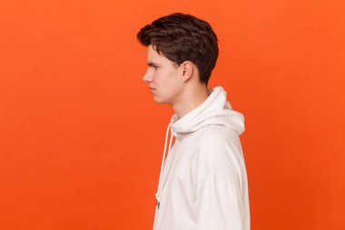 Öne bakan, kendinden emin ve özenli, beyaz kapüşonlu, iddialı genç bir adamın portresi. Turuncu arka planda kapalı stüdyo çekimleri.