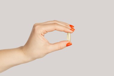 Kadının elinde bitkisel kapsül, besin takviyesi, vitamin hapı ve bitkisel ilaç var. Gri arka planda izole edilmiş kapalı stüdyo görüntüleri.
