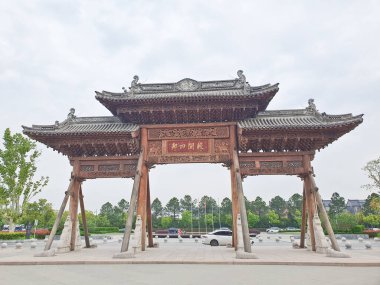 Karmaşık bir şekilde oyulmuş geleneksel Çin ahşap kemer yolu bulutlu bir gökyüzünün altında duruyor, kirişlerle destekleniyor ve heykellerle çevrili. 