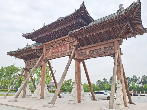 Karmaşık bir şekilde oyulmuş geleneksel Çin ahşap kemer yolu bulutlu bir gökyüzünün altında duruyor, kirişlerle destekleniyor ve heykellerle çevrili. 