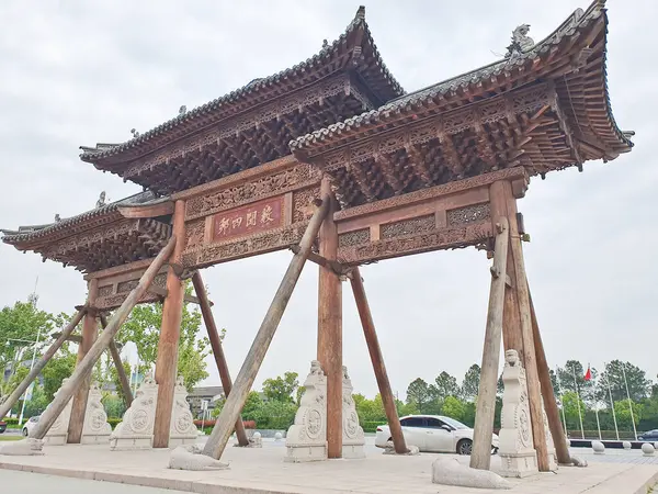 Karmaşık bir şekilde oyulmuş geleneksel Çin ahşap kemer yolu bulutlu bir gökyüzünün altında duruyor, kirişlerle destekleniyor ve heykellerle çevrili. 