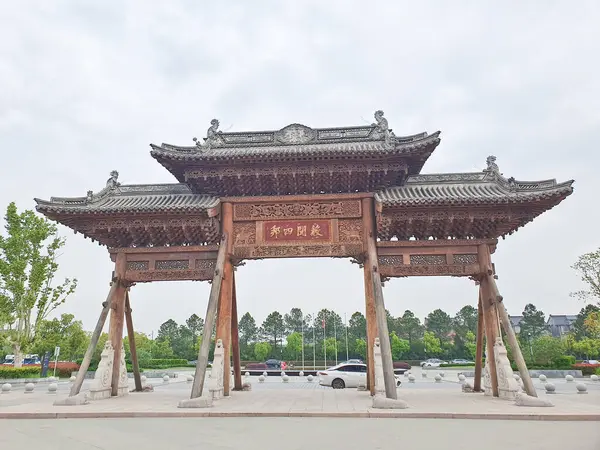 Karmaşık bir şekilde oyulmuş geleneksel Çin ahşap kemer yolu bulutlu bir gökyüzünün altında duruyor, kirişlerle destekleniyor ve heykellerle çevrili. 