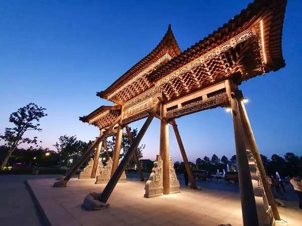 Geleneksel Çin ahşap kemer yolu, alacakaranlıkta aydınlandı, sıcak bir şekilde parlıyordu, ziyaretçiler ve ağaçlarla çevrili, 