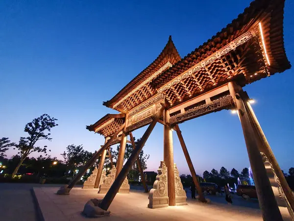 Geleneksel Çin ahşap kemer yolu, alacakaranlıkta aydınlandı, sıcak bir şekilde parlıyordu, ziyaretçiler ve ağaçlarla çevrili, 