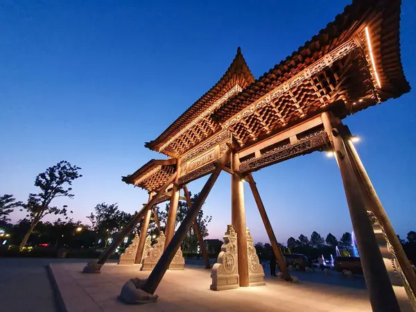 Geleneksel Çin ahşap kemer yolu, alacakaranlıkta aydınlandı, sıcak bir şekilde parlıyordu, ziyaretçiler ve ağaçlarla çevrili, 