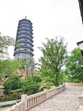 Uzun, süslü bir pagoda geleneksel çatıların üzerinde yükseliyor ve parlak bir gökyüzü altında yemyeşil, huzuru ve tarihi güzelliği simgeliyor.. 