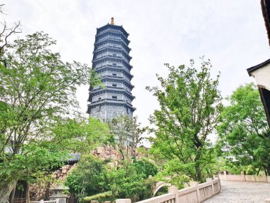 Uzun, süslü bir pagoda geleneksel çatıların üzerinde yükseliyor ve parlak bir gökyüzü altında yemyeşil, huzuru ve tarihi güzelliği simgeliyor.. 