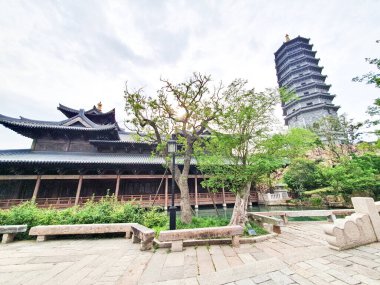 Uzun, süslü bir pagoda geleneksel çatıların üzerinde yükseliyor ve parlak bir gökyüzü altında yemyeşil, huzuru ve tarihi güzelliği simgeliyor.. 