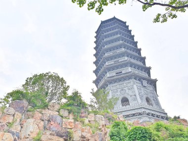 Uzun, süslü bir pagoda geleneksel çatıların üzerinde yükseliyor ve parlak bir gökyüzü altında yemyeşil, huzuru ve tarihi güzelliği simgeliyor.. 