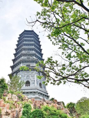 Uzun, süslü bir pagoda geleneksel çatıların üzerinde yükseliyor ve parlak bir gökyüzü altında yemyeşil, huzuru ve tarihi güzelliği simgeliyor.. 
