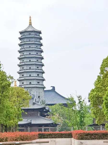 Uzun, süslü bir pagoda geleneksel çatıların üzerinde yükseliyor ve parlak bir gökyüzü altında yemyeşil, huzuru ve tarihi güzelliği simgeliyor.. 
