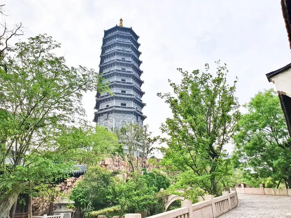 Uzun, süslü bir pagoda geleneksel çatıların üzerinde yükseliyor ve parlak bir gökyüzü altında yemyeşil, huzuru ve tarihi güzelliği simgeliyor.. 