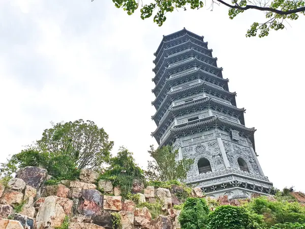 Uzun, süslü bir pagoda geleneksel çatıların üzerinde yükseliyor ve parlak bir gökyüzü altında yemyeşil, huzuru ve tarihi güzelliği simgeliyor.. 