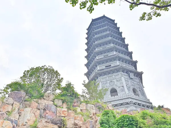 Uzun, süslü bir pagoda geleneksel çatıların üzerinde yükseliyor ve parlak bir gökyüzü altında yemyeşil, huzuru ve tarihi güzelliği simgeliyor.. 