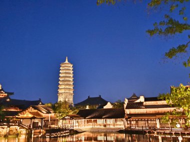 Güzel aydınlatılmış bir pagoda ve geleneksel Çin binaları derin mavi gökyüzünün altındaki sakin suları yansıtır. 