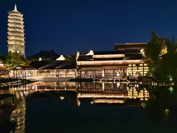 Güzel aydınlatılmış bir pagoda ve geleneksel Çin binaları derin mavi gökyüzünün altındaki sakin suları yansıtır. 