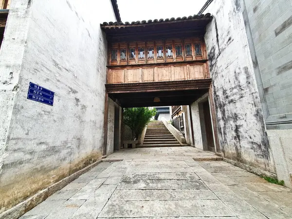 Merdiveni olan dar bir taş yol beyazlatılmış ve gri tuğlalı duvarlar arasındaki geleneksel Çin ahşap koridor köprüsünün altına çıkıyor. 