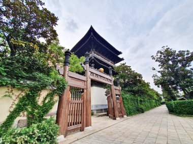 Karmaşık oymalar ve ahşap kapılar ile süslü geleneksel bir Çin taş kemer yolu ağaçlarla kaplı sessiz bir sokağa açılıyor. 