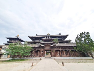 Görkemli, çok katmanlı ahşap bir tapınak. Karmaşık çatı sahaları ve geleneksel oymalar bulutlu bir arka planda duruyor. 