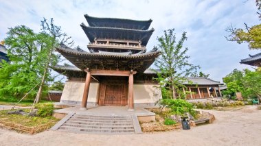 Görkemli, çok katmanlı ahşap bir tapınak. Karmaşık çatı sahaları ve geleneksel oymalar bulutlu bir arka planda duruyor. 