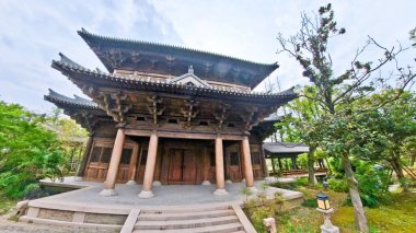 Görkemli, çok katmanlı ahşap bir tapınak. Karmaşık çatı sahaları ve geleneksel oymalar bulutlu bir arka planda duruyor. 