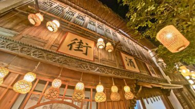 Geleneksel Çin ahşap binası, üzerinde parıldayan fenerlerle aydınlatılmış, ılık, şenlikli bir gece ortamı yaratıyor. 