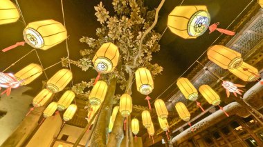 Düzinelerce parıldayan geleneksel fener bir gece sokağının üzerinde asılı, dekoratif balık süslemeleriyle sıcak ve şenlikli bir ortam yaratıyor. 