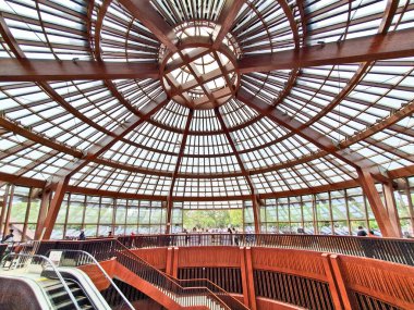 Büyük ahşap bir kubbe ve cam panelleri olan, aşağıda yürüyen ve etkileşen ziyaretçilerin yer aldığı geniş bir kapalı bina. 