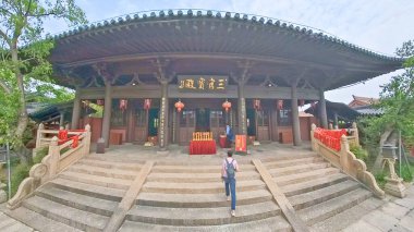 Geleneksel Çin tapınağı, kırmızı fenerler, taş tütsü yakıcı, ve hat plaketi, parlak mavi gökyüzünün altında yeşilliklerle çevrili.. 