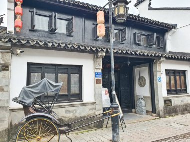 Geleneksel Çin binası, siyah ahşap pencereler, kırmızı fenerler, ve sessiz bir caddede park edilmiş klasik bir triportör. 