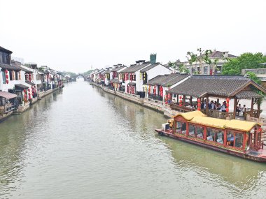 Geleneksel bir kanal kasabası, kırmızı fenerler, beyazlatılmış binalar ve sisli bir gökyüzünün altında huzur içinde süzülen manzaralı bir tekne. 