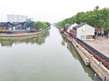 Geleneksel bir kanal kasabası, kırmızı fenerler, beyazlatılmış binalar ve sisli bir gökyüzünün altında huzur içinde süzülen manzaralı bir tekne. 