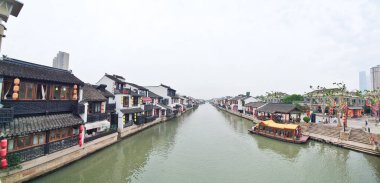 Geleneksel bir kanal kasabası, kırmızı fenerler, beyazlatılmış binalar ve sisli bir gökyüzünün altında huzur içinde süzülen manzaralı bir tekne. 