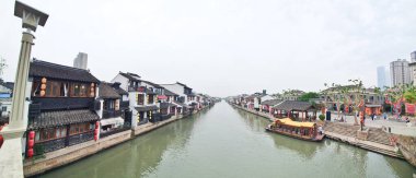 Geleneksel bir kanal kasabası, kırmızı fenerler, beyazlatılmış binalar ve sisli bir gökyüzünün altında huzur içinde süzülen manzaralı bir tekne. 