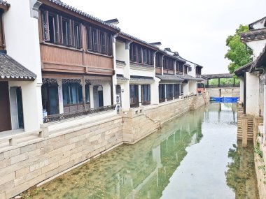 Geleneksel bir kanal kasabası, kırmızı fenerler, beyazlatılmış binalar ve sisli bir gökyüzünün altında huzur içinde süzülen manzaralı bir tekne. 