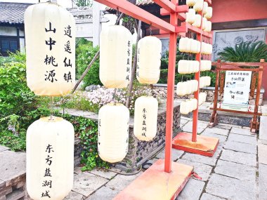 Yeşil yapraklar ve sergilenen Çince karakterlerle çevrili düzinelerce dokuma sarı fener bambu bir çerçeveye asılmış. 