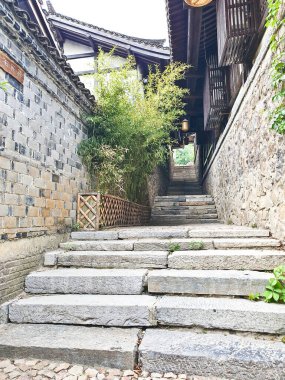 Geleneksel ahşap binalarla çevrili ve yemyeşil ağaçlarla gölgelenmiş sakin bir ara sokakta taş bir patika esiyor. 