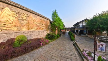 Bereketli yeşillik ve geleneksel mimariyle çevrili, dağ oymalarıyla dekoratif bir duvarın yanında huzurlu bir taş yol uzanıyor. 