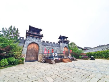 Ahşap kapılar, fenerler, bekçi kuleleri ve çevresindeki yeşilliklerle dolu kadim taş kale kapısı, parlak bulutlu bir gökyüzü altında.. 