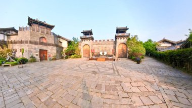 Ahşap kapılar, fenerler, bekçi kuleleri ve çevresindeki yeşilliklerle dolu kadim taş kale kapısı, parlak bulutlu bir gökyüzü altında.. 