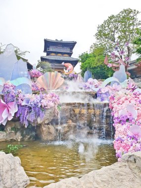 Pastel süslemeli güzel bir çeşme, çağlayan su, ve canlı çiçekler ve sisle çevrili geleneksel bir Asya tapınağı. 