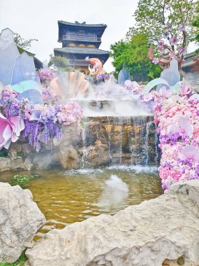 Pastel süslemeli güzel bir çeşme, çağlayan su, ve canlı çiçekler ve sisle çevrili geleneksel bir Asya tapınağı. 