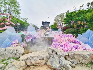 Pastel süslemeli güzel bir çeşme, çağlayan su, ve canlı çiçekler ve sisle çevrili geleneksel bir Asya tapınağı. 