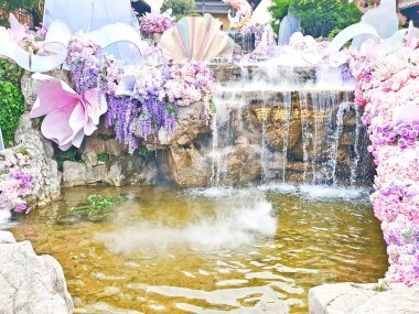 Pastel süslemeli güzel bir çeşme, çağlayan su, ve canlı çiçekler ve sisle çevrili geleneksel bir Asya tapınağı. 