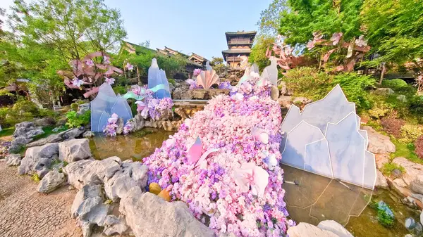 Çin yazıtlı geleneksel bir taş çeşme bitkiler, çiçekler ve ahşap elementlerle çevrili eski bir binaya karşı kurulur. 