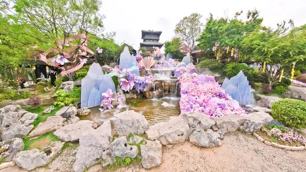 Çin yazıtlı geleneksel bir taş çeşme bitkiler, çiçekler ve ahşap elementlerle çevrili eski bir binaya karşı kurulur. 