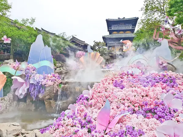 Pastel süslemeli güzel bir çeşme, çağlayan su, ve canlı çiçekler ve sisle çevrili geleneksel bir Asya tapınağı. 