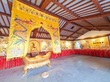 Geleneksel bir tapınakta altın bir tanrı heykeli, süslü sarı ejderha afişi, kırmızı dua kurdeleleri ve karmaşık duvar oymaları yer alıyor. 